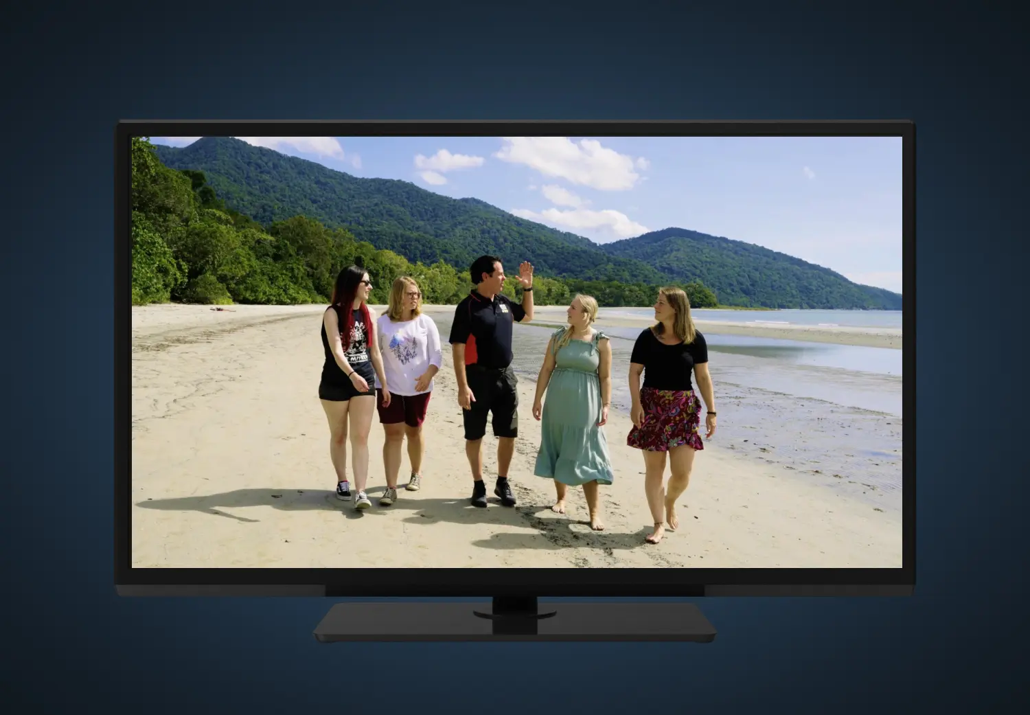A group of people standing on a beach in front of a tv
