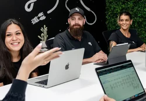 A group of people sitting around a table with laptops