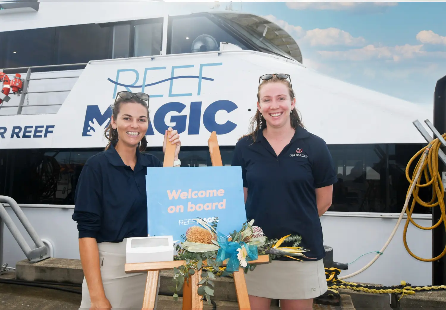 Two women standing in front of a boat holding a welcome sign