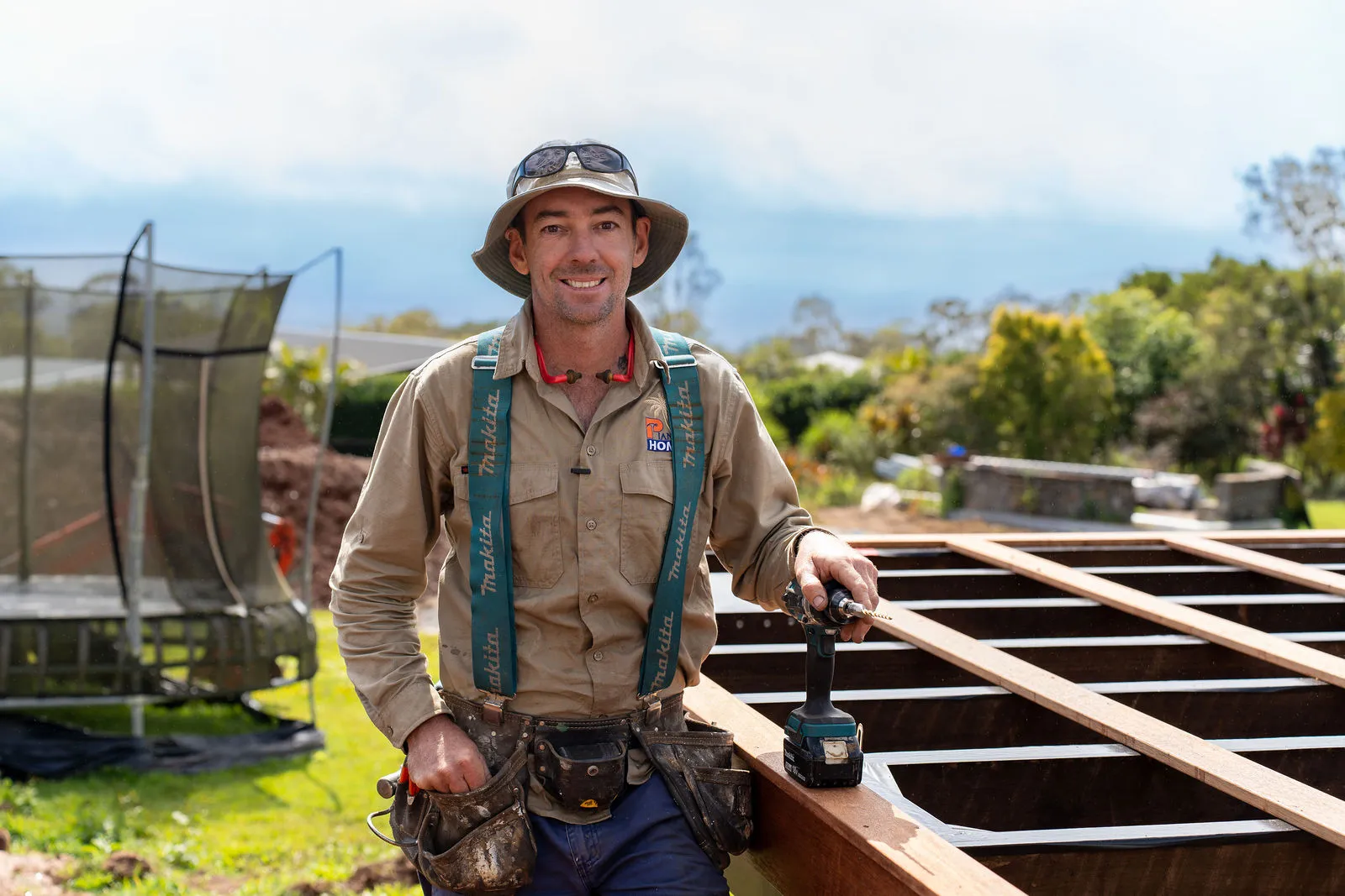 A deck builder on a timber frame holding a drill fitted with the NOGBOSS assembly