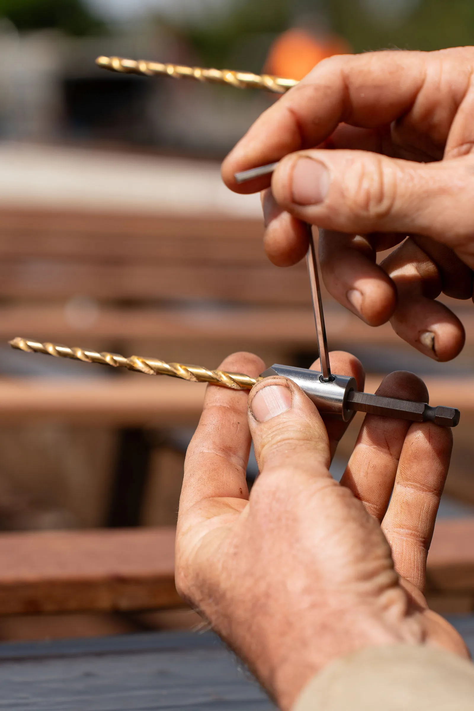 Hands holding NOGBOSS drill bit assemblies on a job site